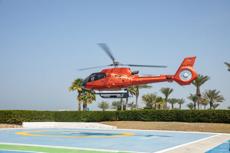 Interior view of a helicopter cockpit with pilot controls and panoramic cityscape through the windshield.
